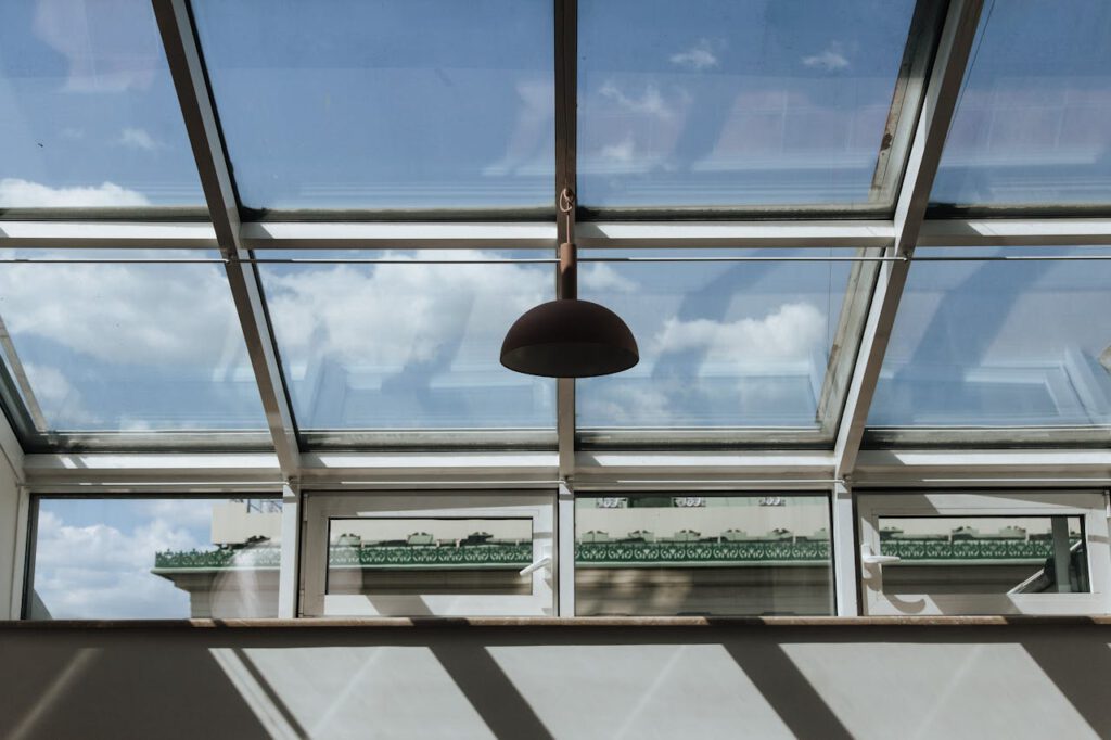 pexels-photo-10222724 Vertical shot of a modern glass ceiling with clear sky and a hanging lamp, showcasing architectural elegance.