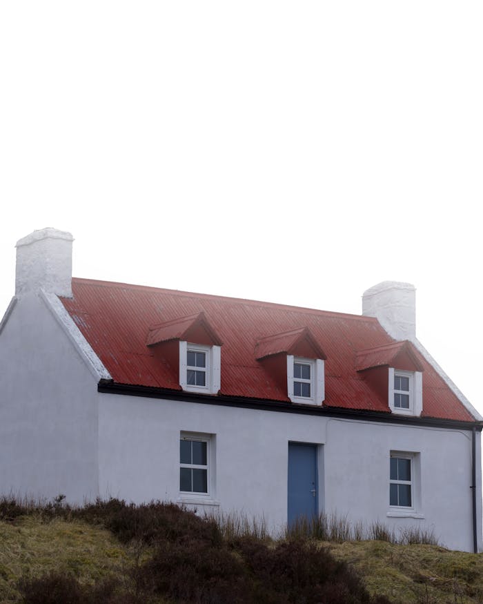 pexels-photo-27367295 Charming white cottage with red roof in Scotland set against cloudy skies.